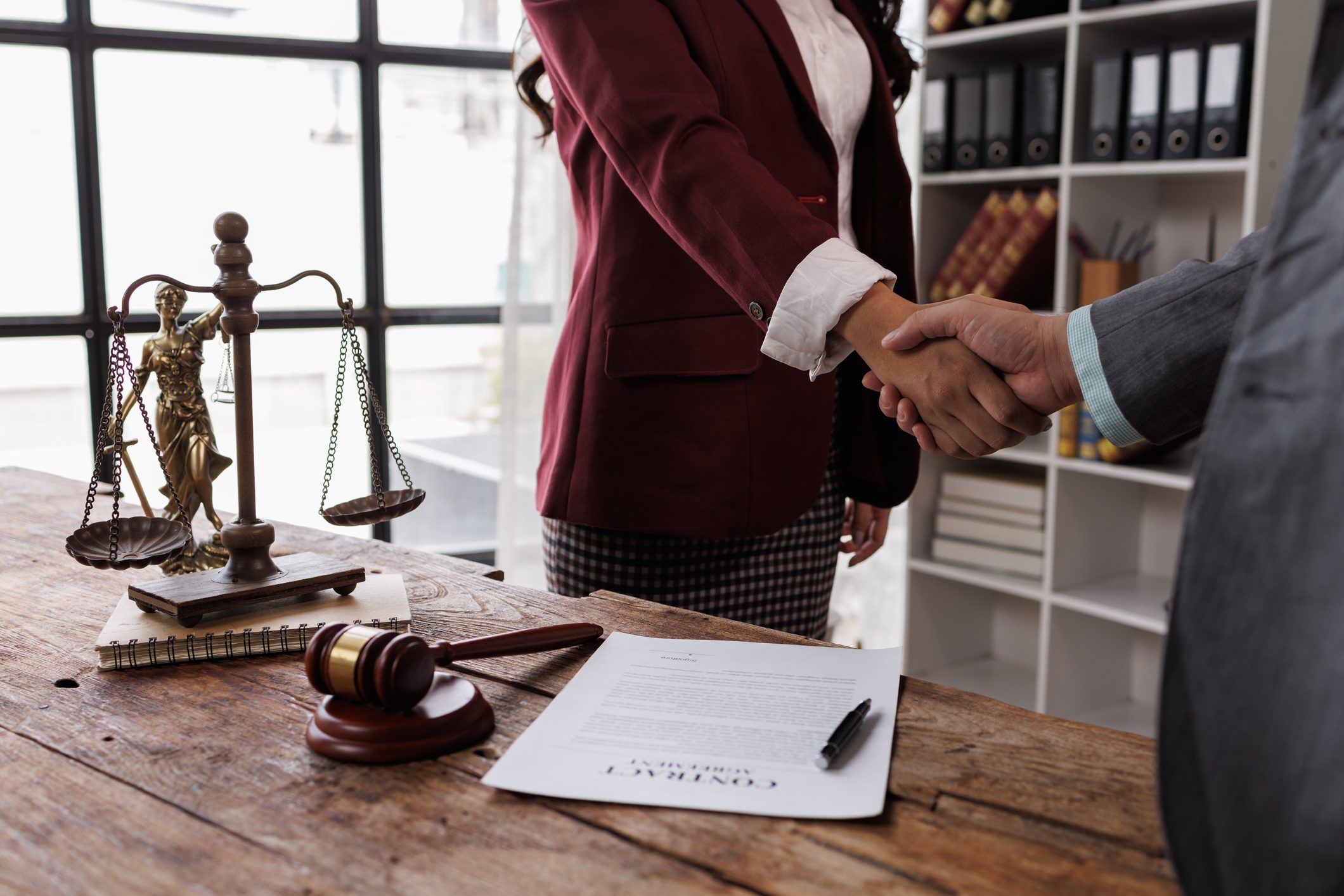 Professional Lawyer Handshake in Business Meeting with Scales of Justice and Gavel on Desk, Symbolizing Legal Agreement and Partnership attorneys discussing a contract agreement.