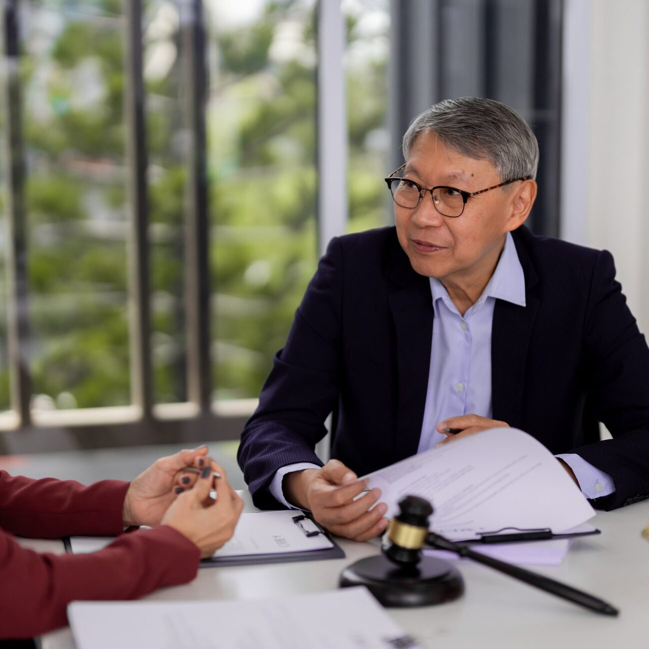 Expert Asian lawyers and adult clients engage in a focused legal consultation reviewing crucial documents seeking advice and justice in a contemporary office